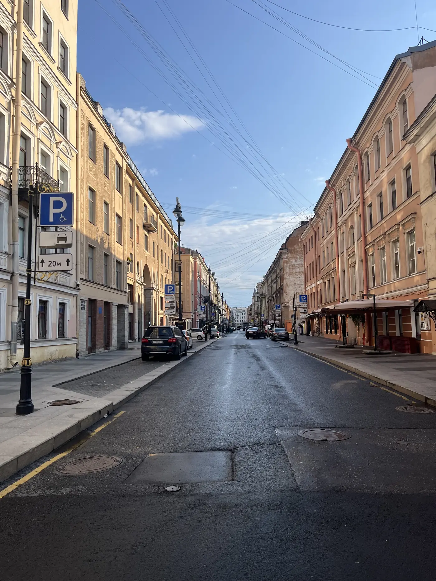 Empty early-morning St. Petersburg street lined with pastel neoclassical apartment buildings, parked cars, and a warm sunrise glow