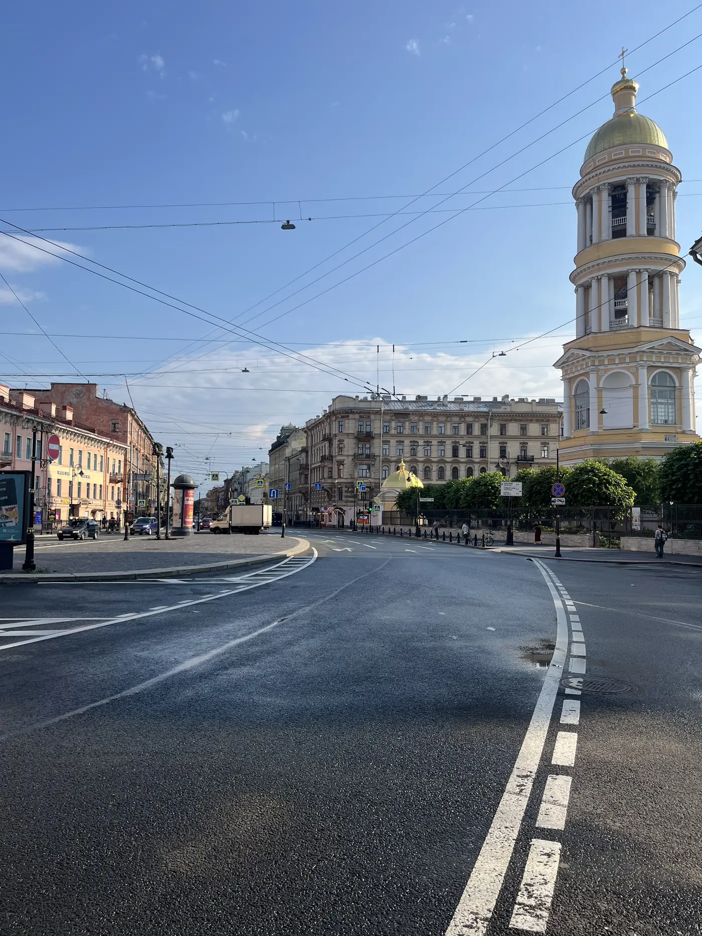 Empty early-morning St. Petersburg street with trolleybus wires, neoclassical buildings and a yellow church bell tower with gold dome in the distance