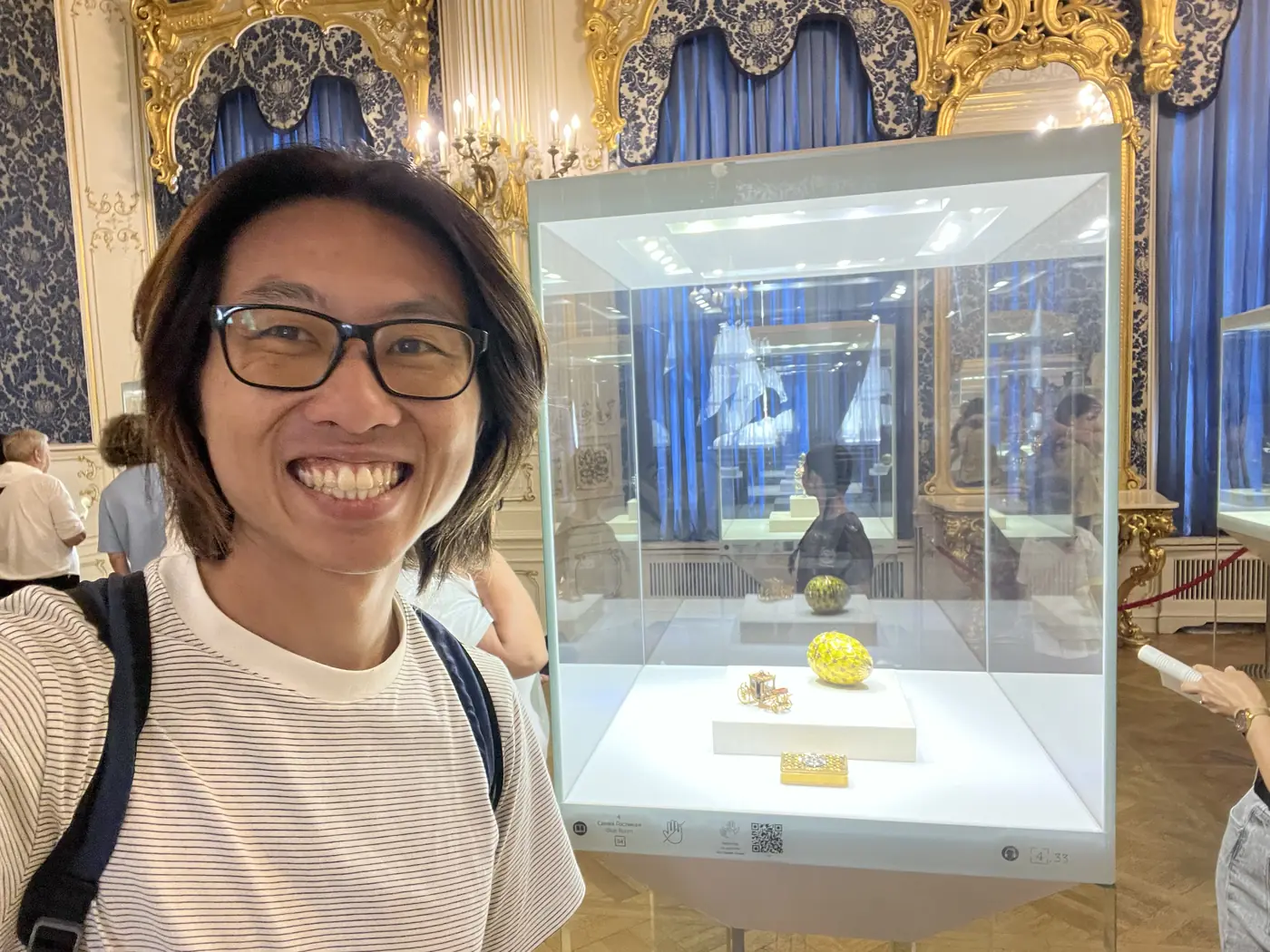 Shin selfie inside the Fabergé Museum with a yellow Fabergé egg in a glass case behind him, ornate gold baroque room with blue curtains