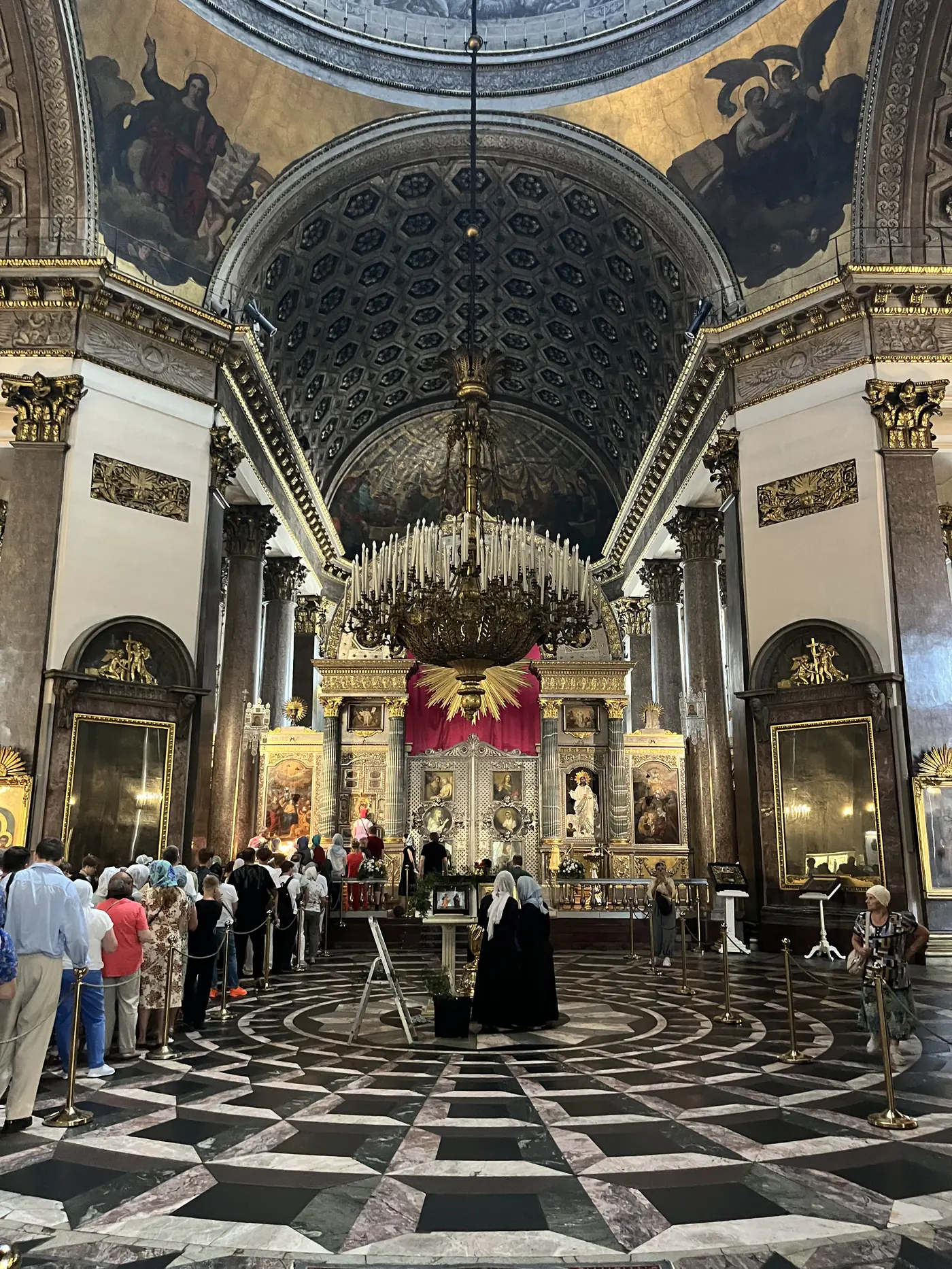 Grand gilded interior of St. Isaac's Cathedral in St. Petersburg, with a soaring painted dome, marble columns, and visitors queuing near the altar