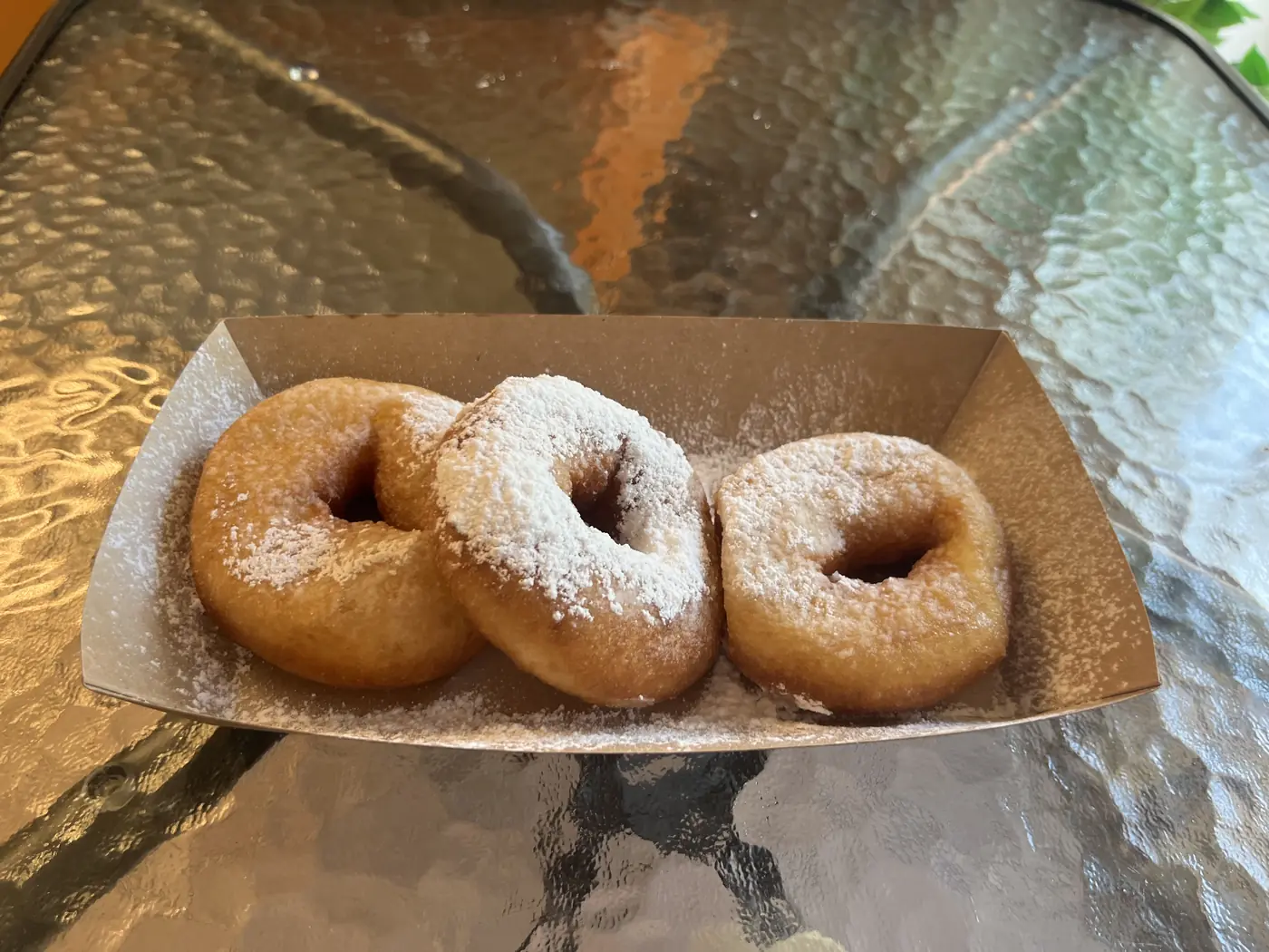 Three powdered-sugar fried donuts, pyshki, served in a paper tray on a St. Petersburg café table