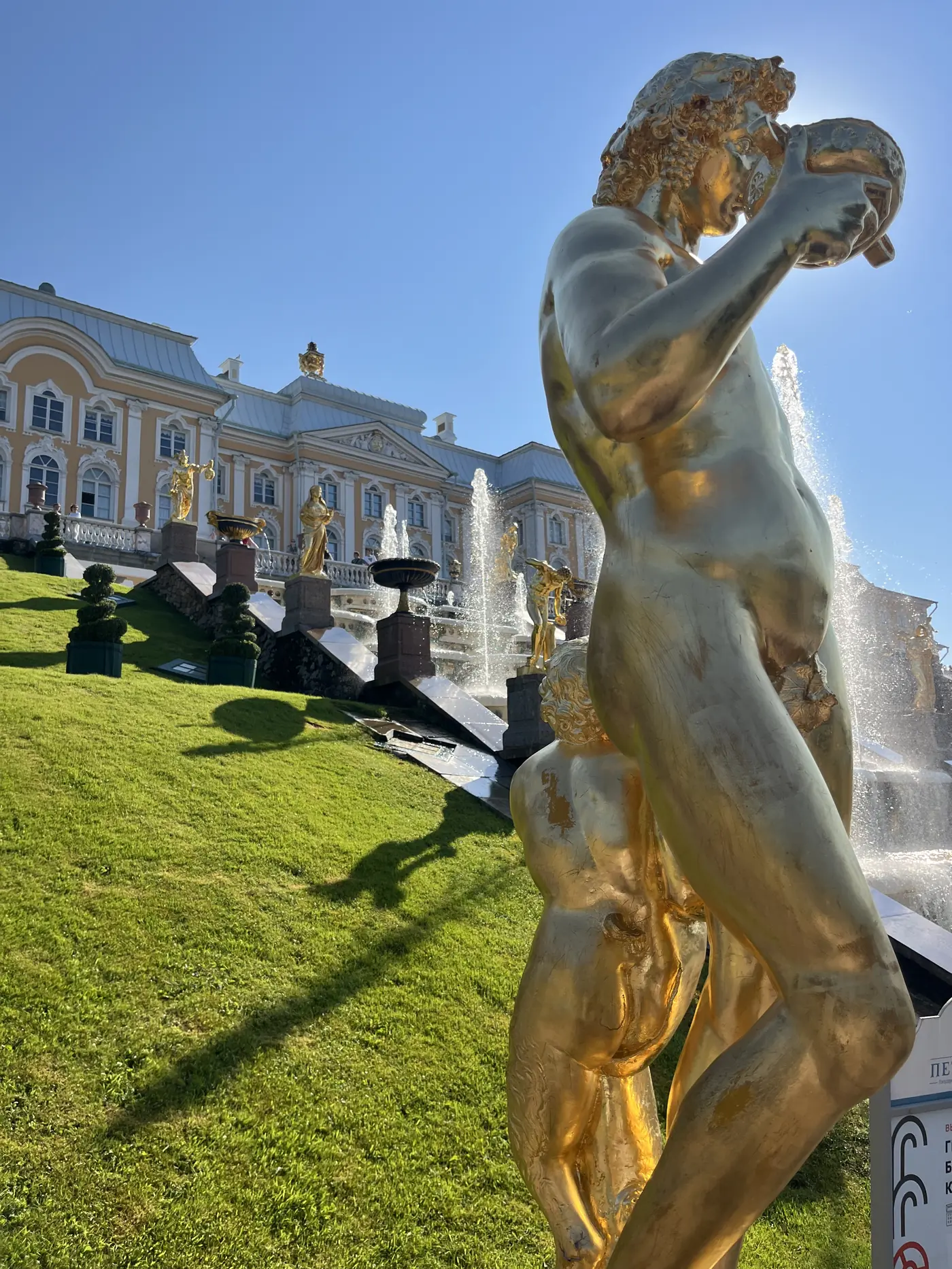 Close-up of a gilded baroque statue at Peterhof's Grand Cascade holding a lion's jaw open, with the palace facade and fountains cascading behind