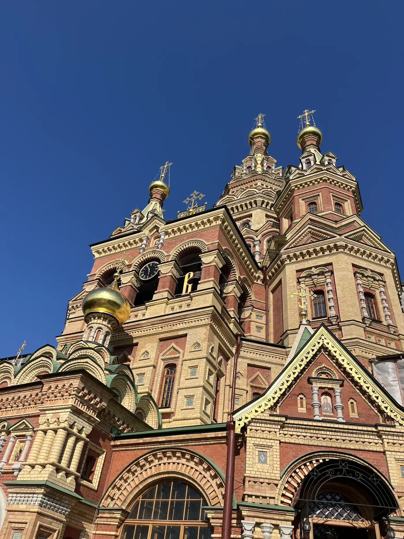 The colourful red-brick Cathedral of Saints Peter and Paul in the Peterhof palace grounds, with golden onion domes against a clear blue sky