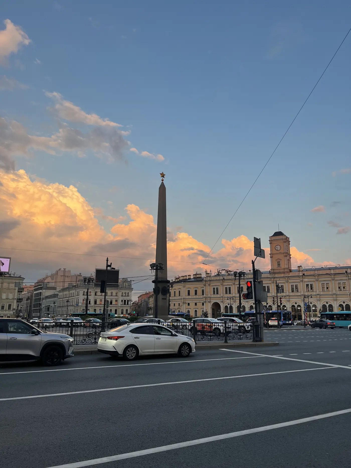 Sunset over Vosstaniya Square in St. Petersburg with a Soviet granite obelisk topped by a red star and the Moskovsky railway station clock tower, dramatic pink clouds