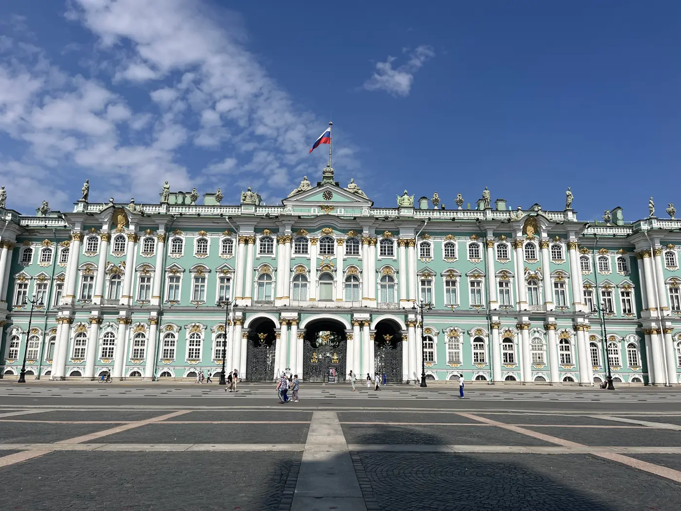 The Winter Palace's turquoise and white baroque facade on Palace Square, St. Petersburg, under a bright blue sky