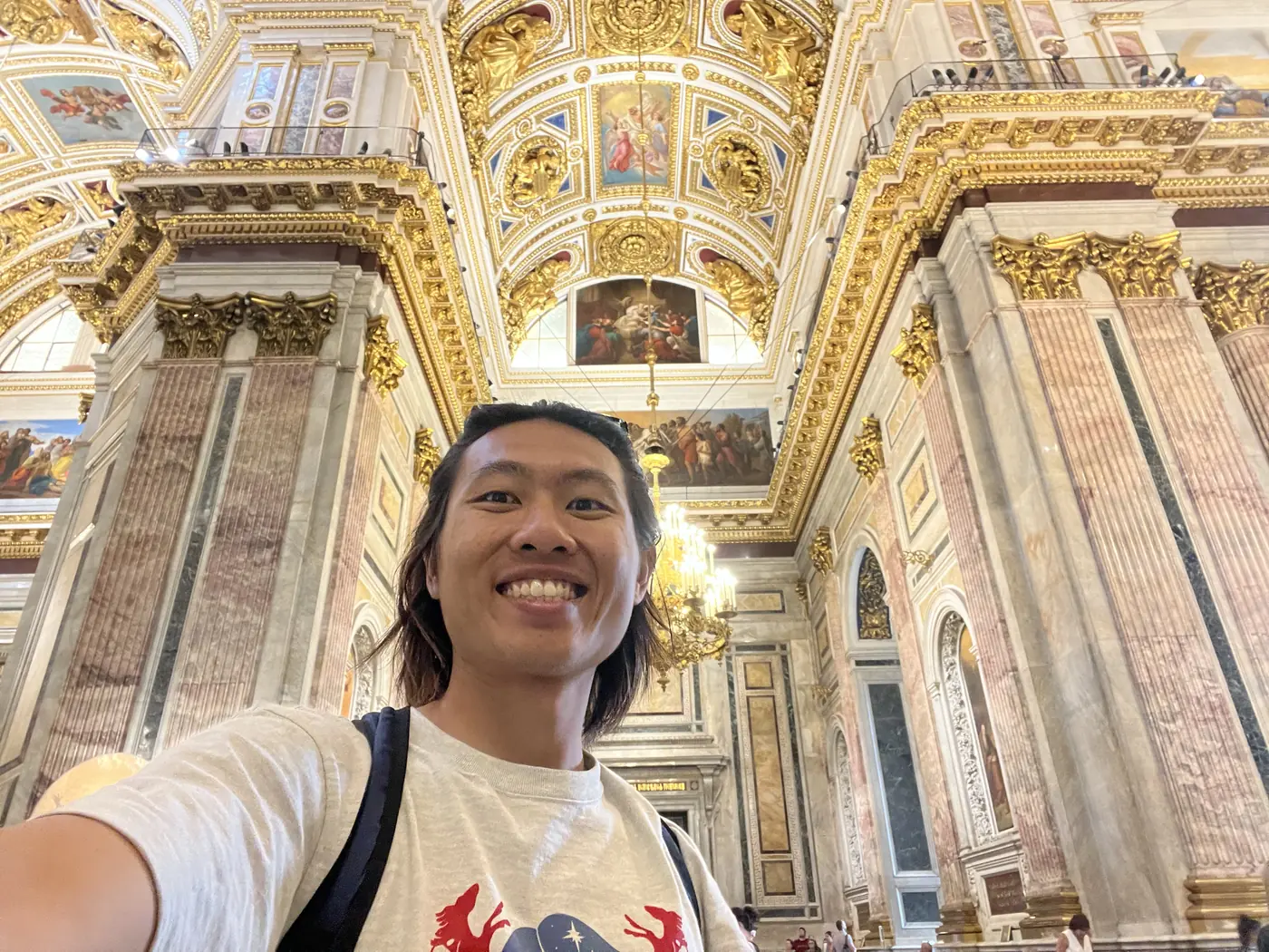 Shin selfie inside St. Isaac's Cathedral, St. Petersburg, with gilded arches, marble columns, and painted ceiling panels surrounding him
