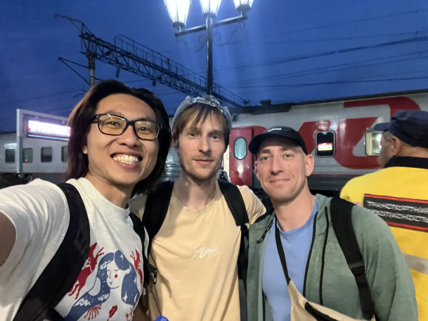 Shin with two Western backpackers on Trans-Siberian Railway platform at night in Ulan-Ude, red RZhD train behind them