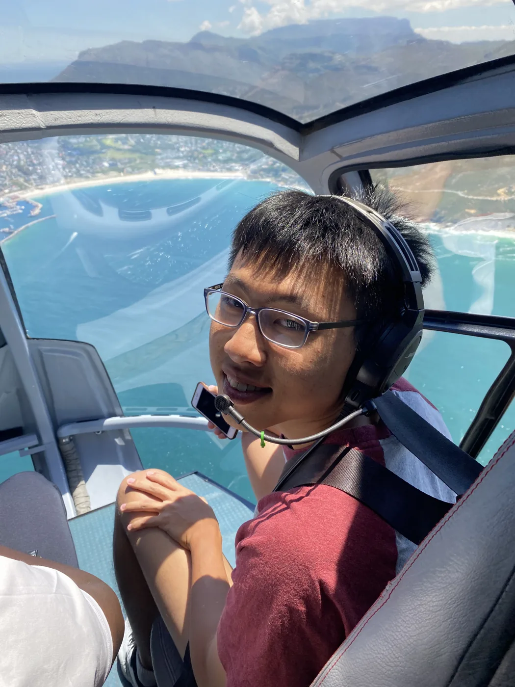 Smiling in a helicopter with headset on, turquoise Cape Town coastline below