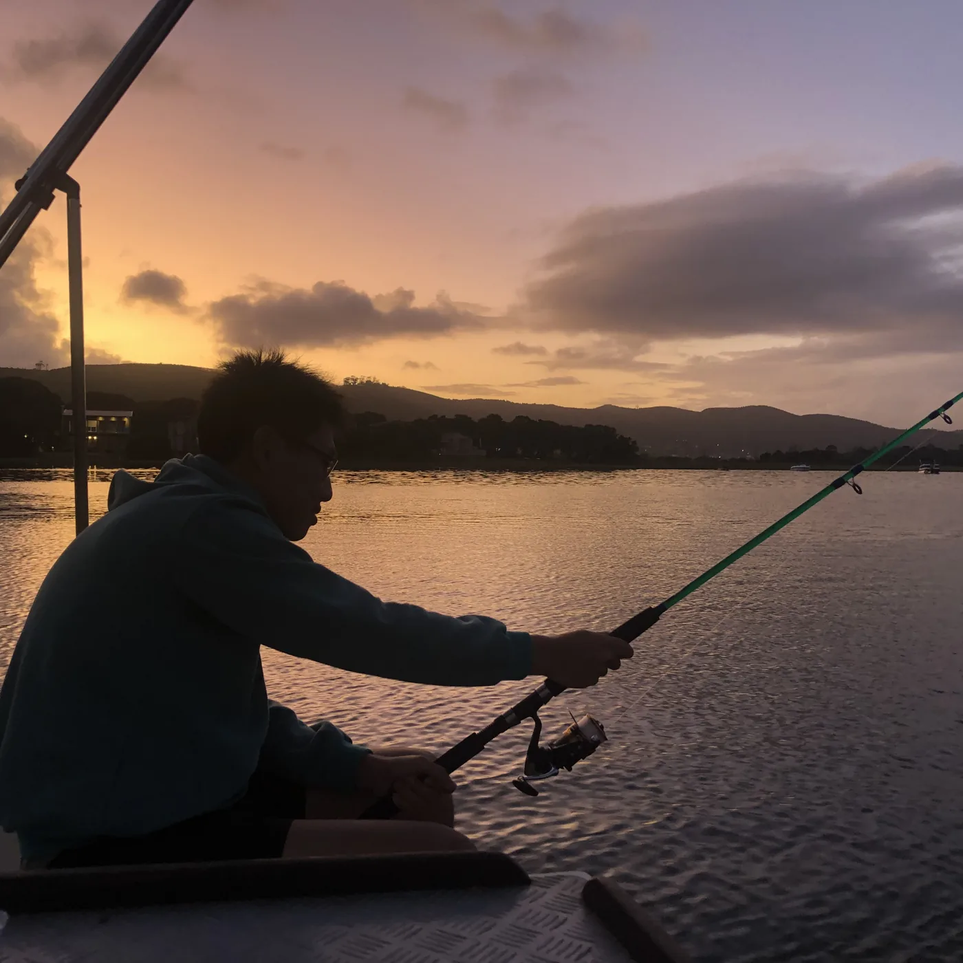 Silhouette fishing from a boat at golden sunset over a calm lagoon