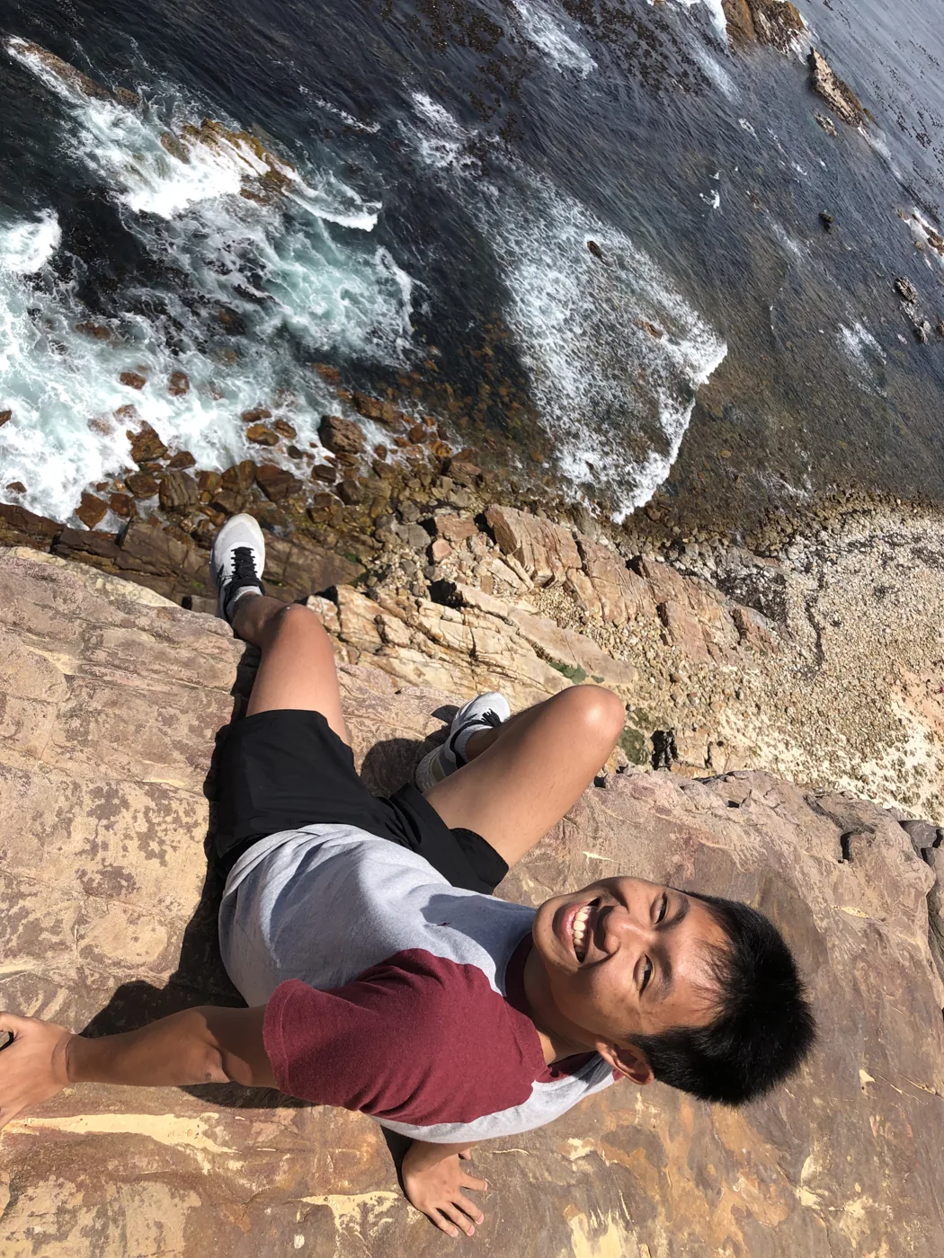 Lying on the cliff edge at Cape Point, waves crashing on the rocks far below