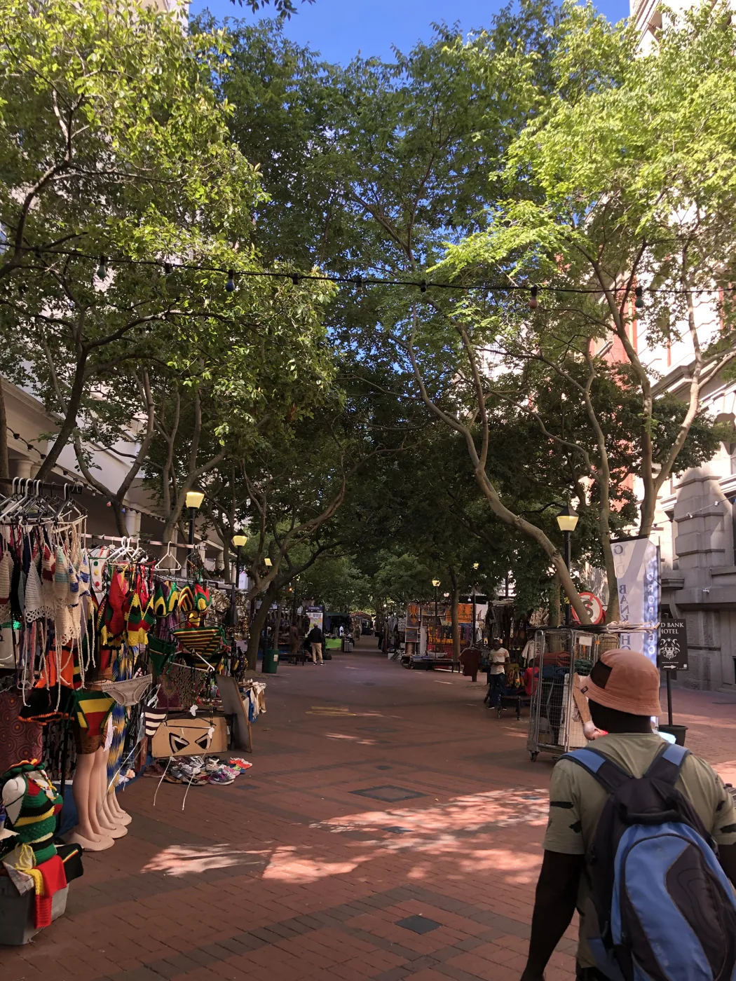 Walking through Greenmarket Square craft market under leafy trees in Cape Town
