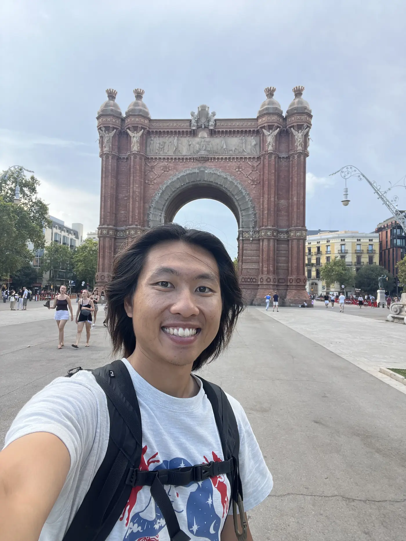 Shin selfie in front of the Arc de Triomf, a red-brick triumphal arch in Barcelona, with a wide plaza behind him