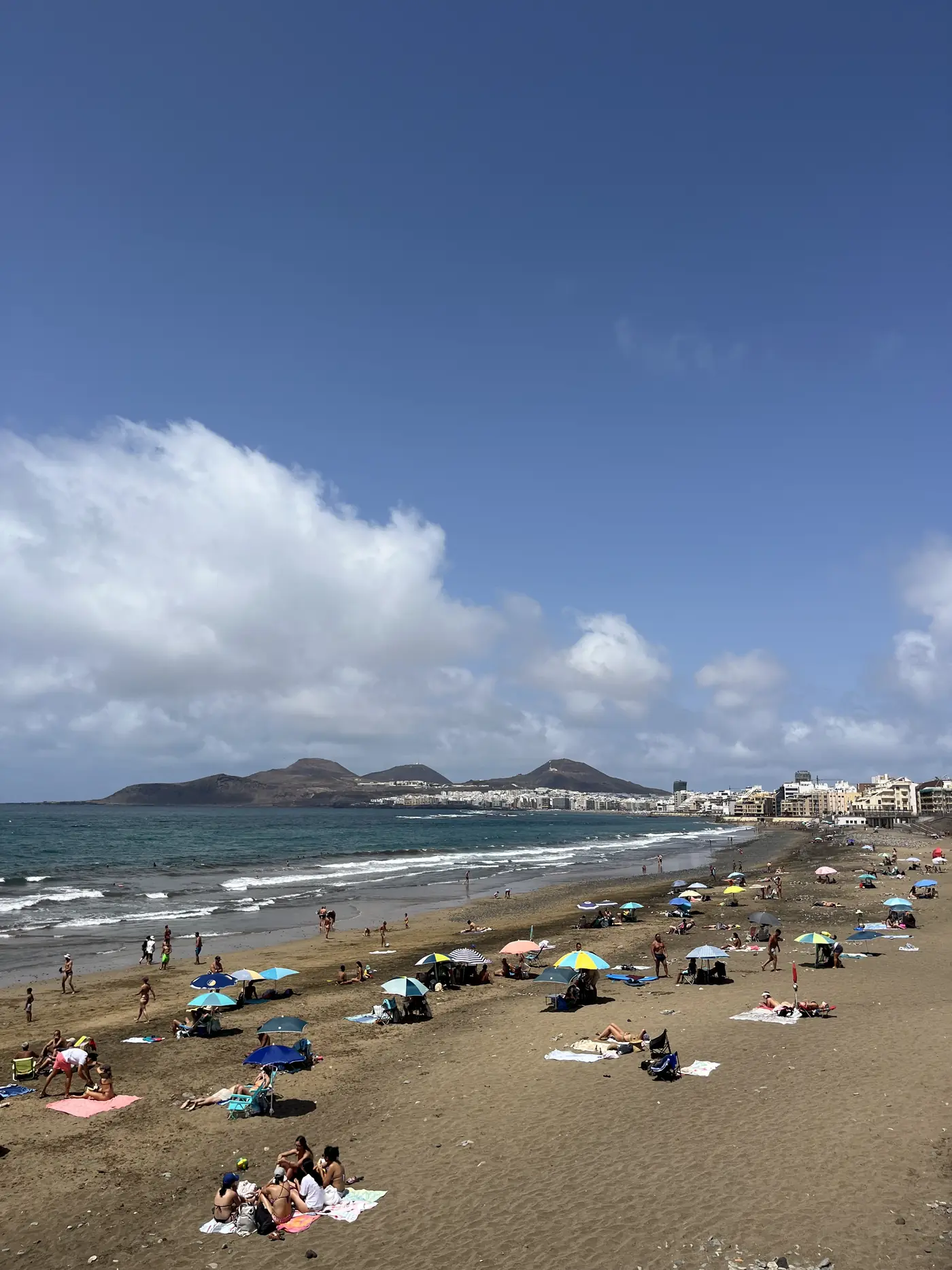 Playa de Las Canteras beach in Las Palmas, Gran Canaria, sunbathers and umbrellas along golden sand with a volcanic hill in the distance