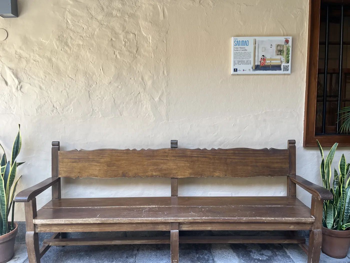A wooden bench beneath a Sanmao commemorative plaque in a shaded courtyard in Gran Canaria