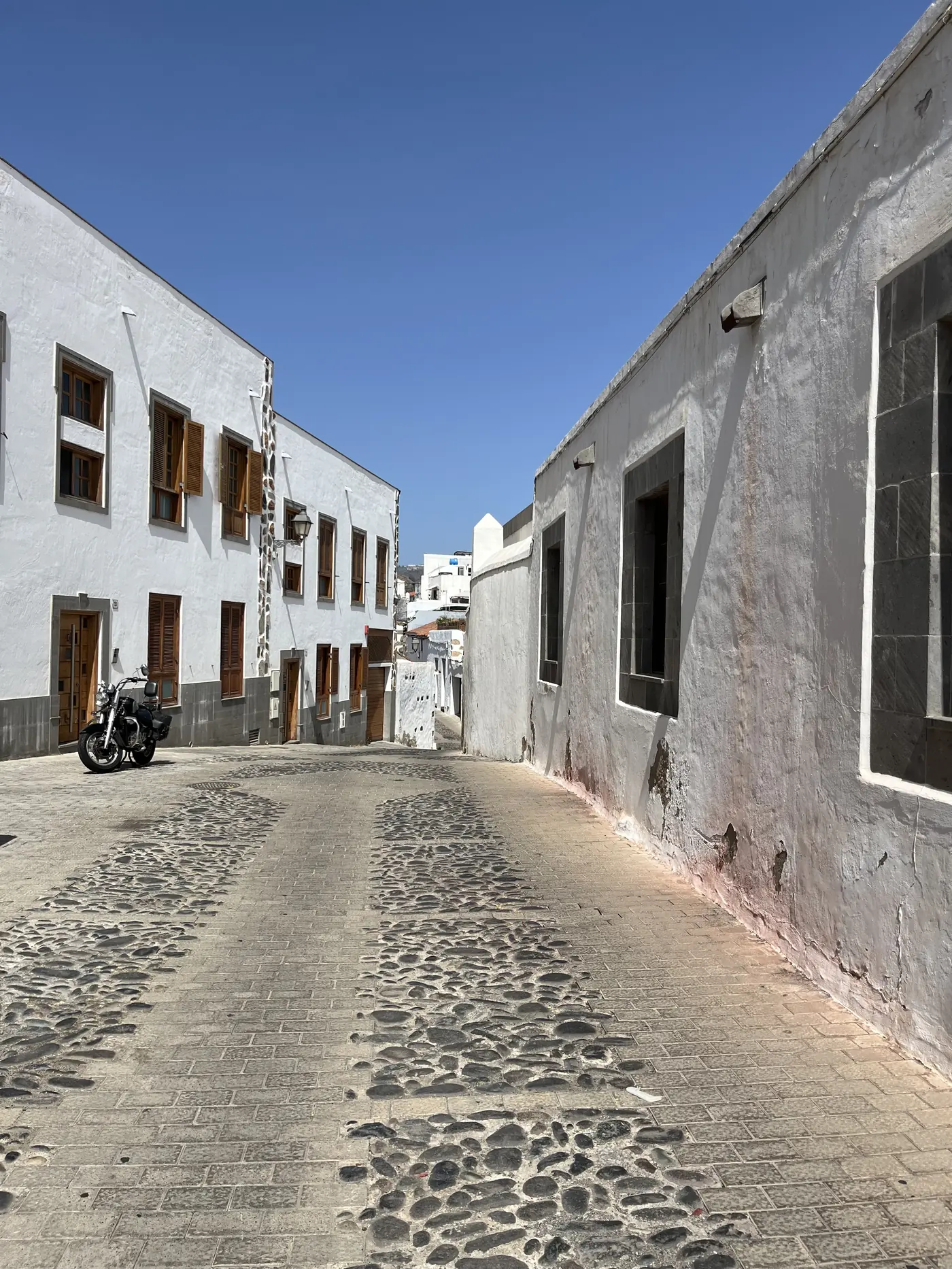 A whitewashed Canarian village street with shuttered windows and a parked motorbike, part of the Ruta Sanmao walking route