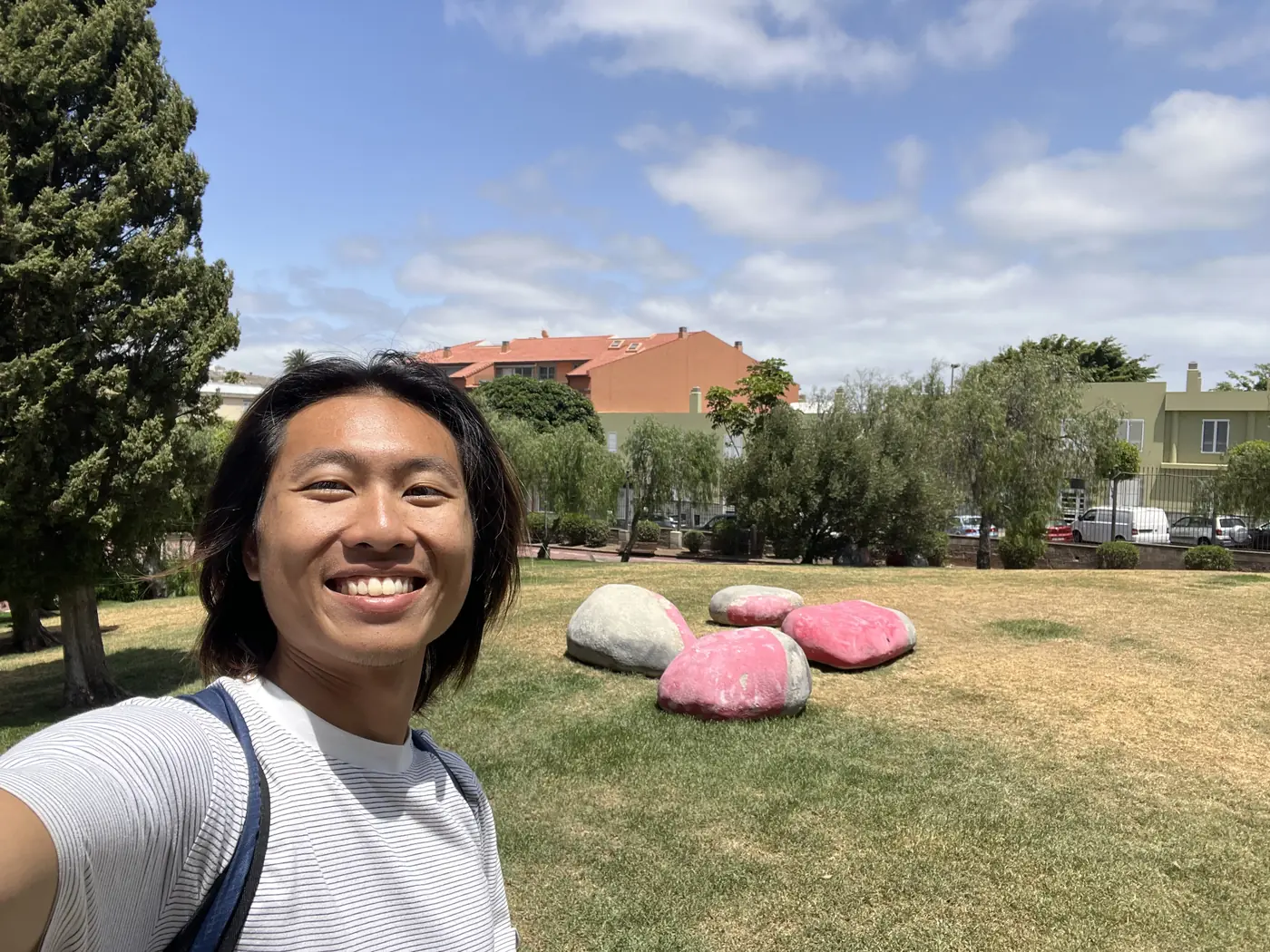Shin smiling in a park in Gran Canaria with large painted boulder sculptures on the lawn behind him