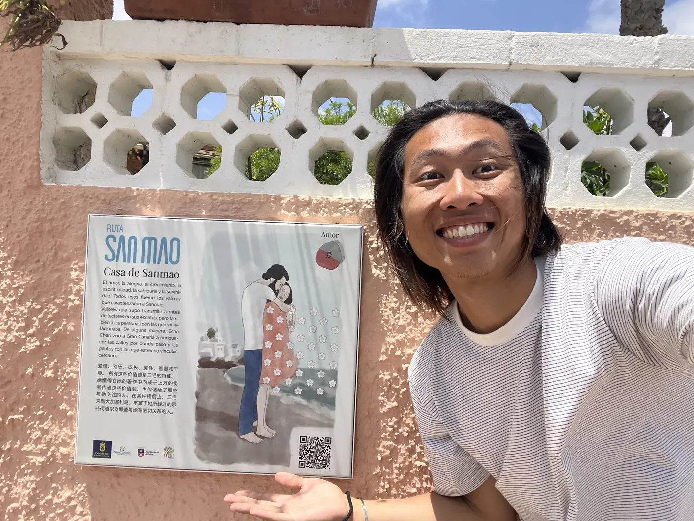 Shin smiling in front of a 'Ruta San Mao — Casa de Sanmao' sign mounted on a decorative wall in Gran Canaria