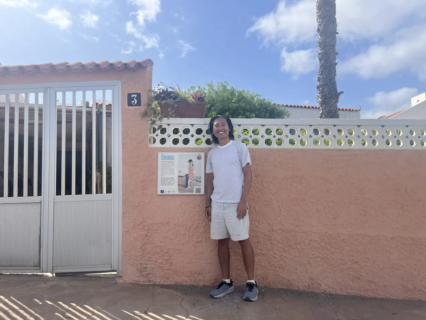 Shin standing outside the pink garden wall and gate of Casa de Sanmao, house number 3, in Gran Canaria