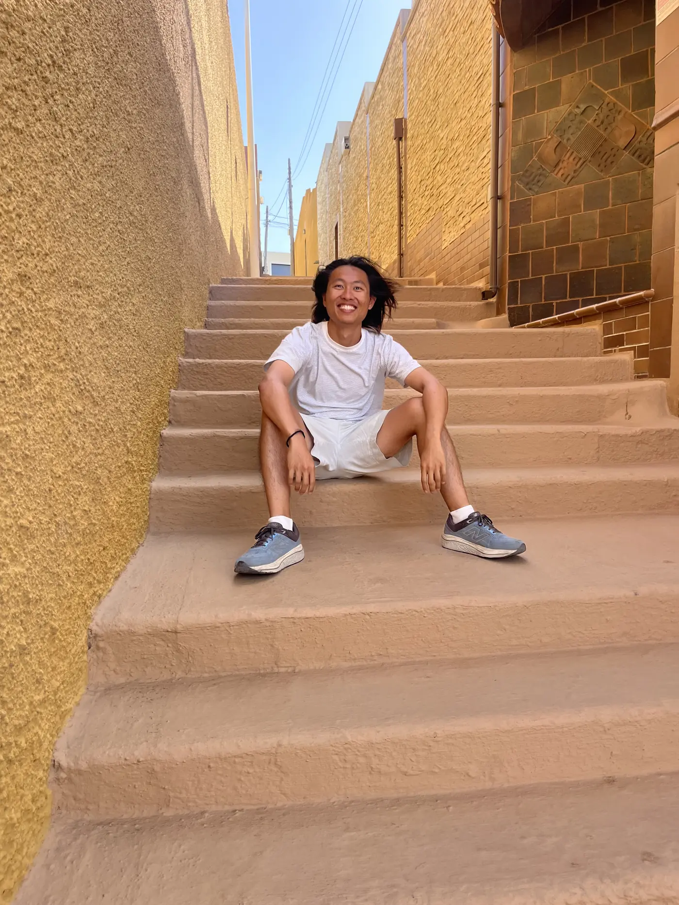 Shin sitting and smiling on sunlit sandstone-coloured steps in a narrow alley near Sanmao's former house in Gran Canaria