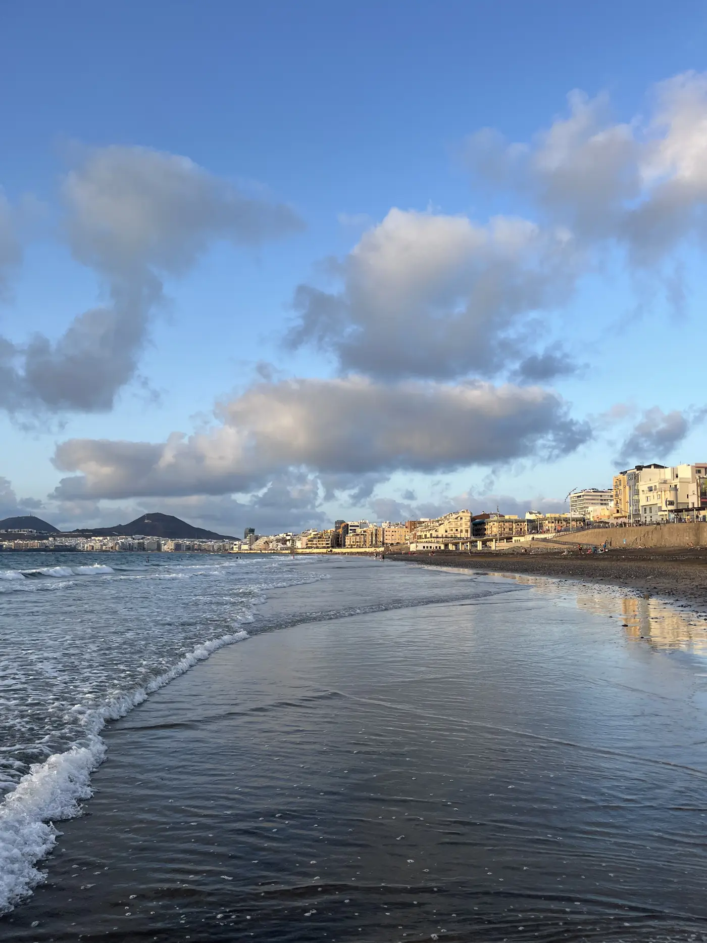 Evening view along Playa de Las Canteras, Las Palmas, with soft clouds over the water and beachfront buildings in the distance