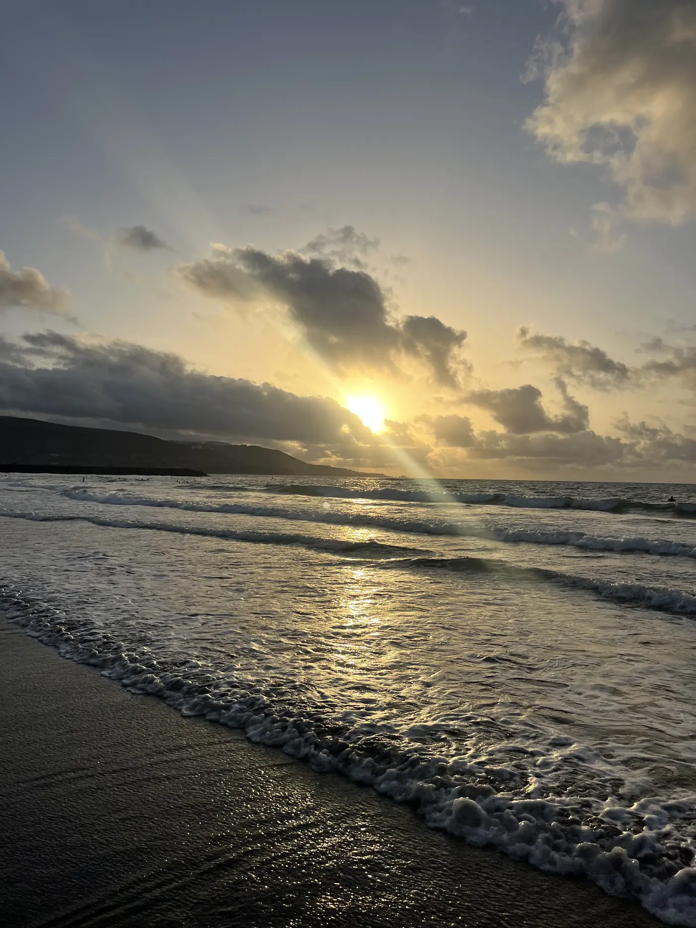 Sunset over the ocean at Playa de Las Canteras, sun breaking through clouds with rays reflecting on the waves