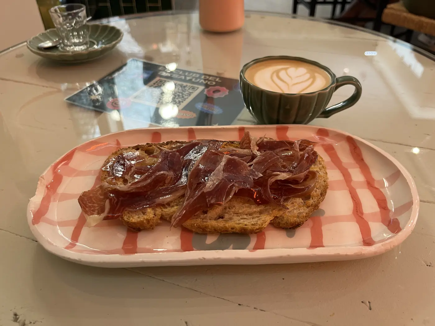 Jamón ibérico toast and a café con leche with latte art on a marble café table in Las Palmas, Gran Canaria