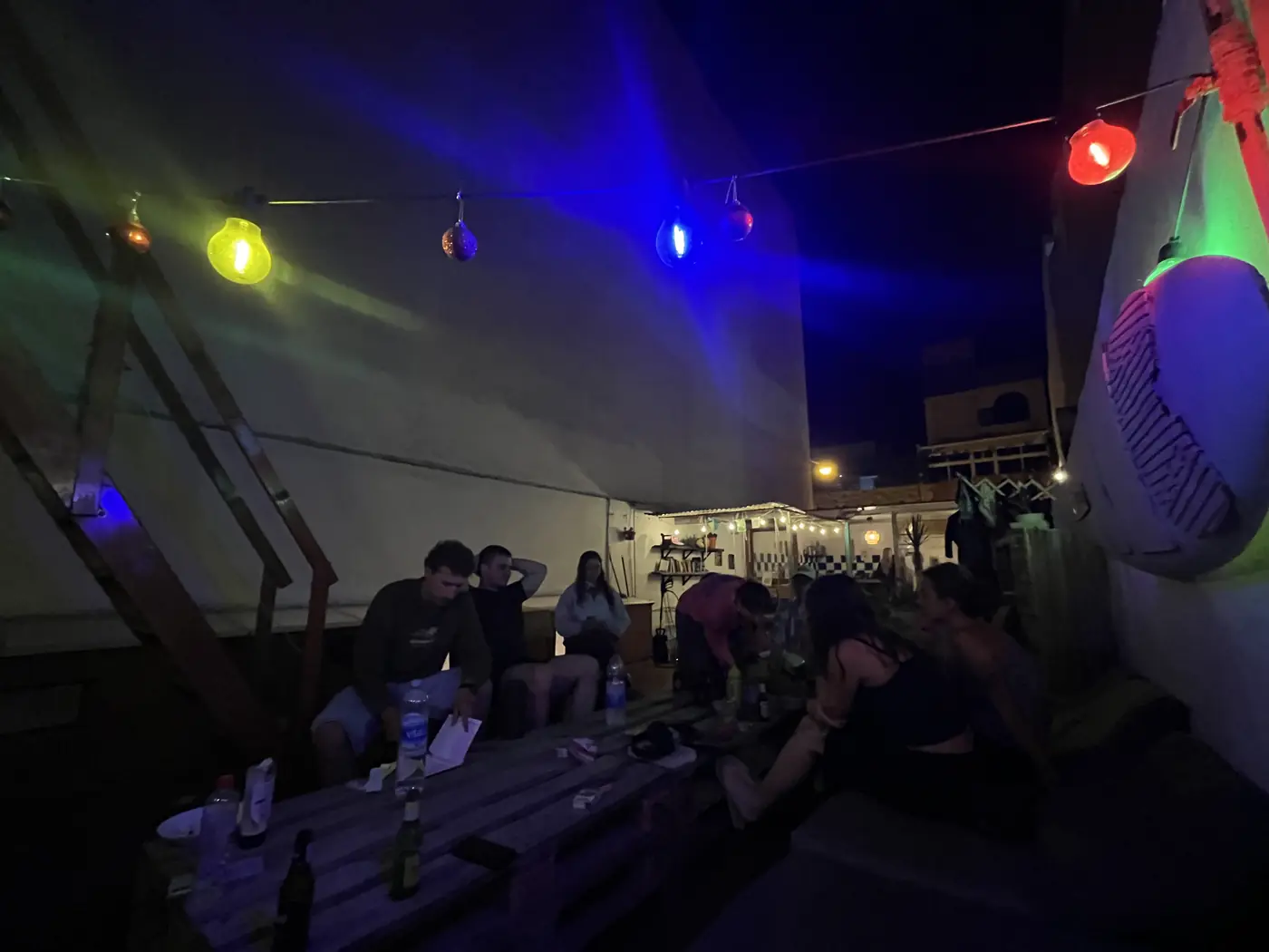 A nighttime rooftop bar scene in Gran Canaria with colourful string lights and people gathered around a wooden table