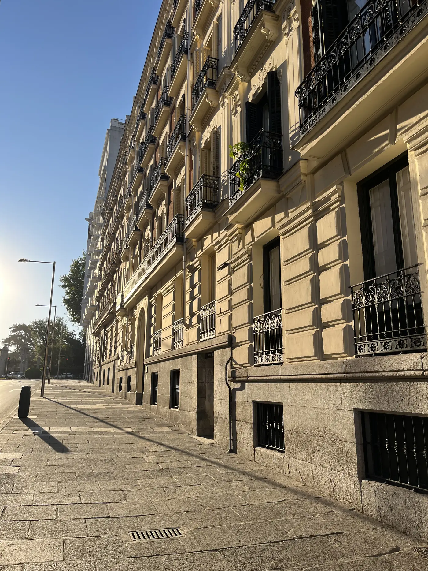 Early morning Madrid street lined with ornate 19th-century buildings and black wrought-iron balconies, low sunlight casting long shadows