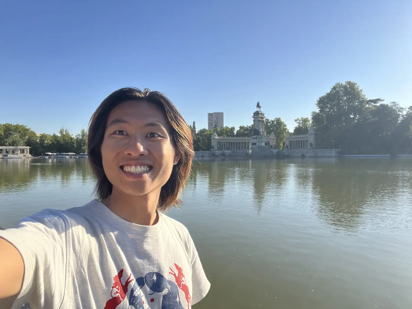 Shin selfie by the lake in Retiro Park, Madrid, with the Monument to Alfonso XII visible across the water