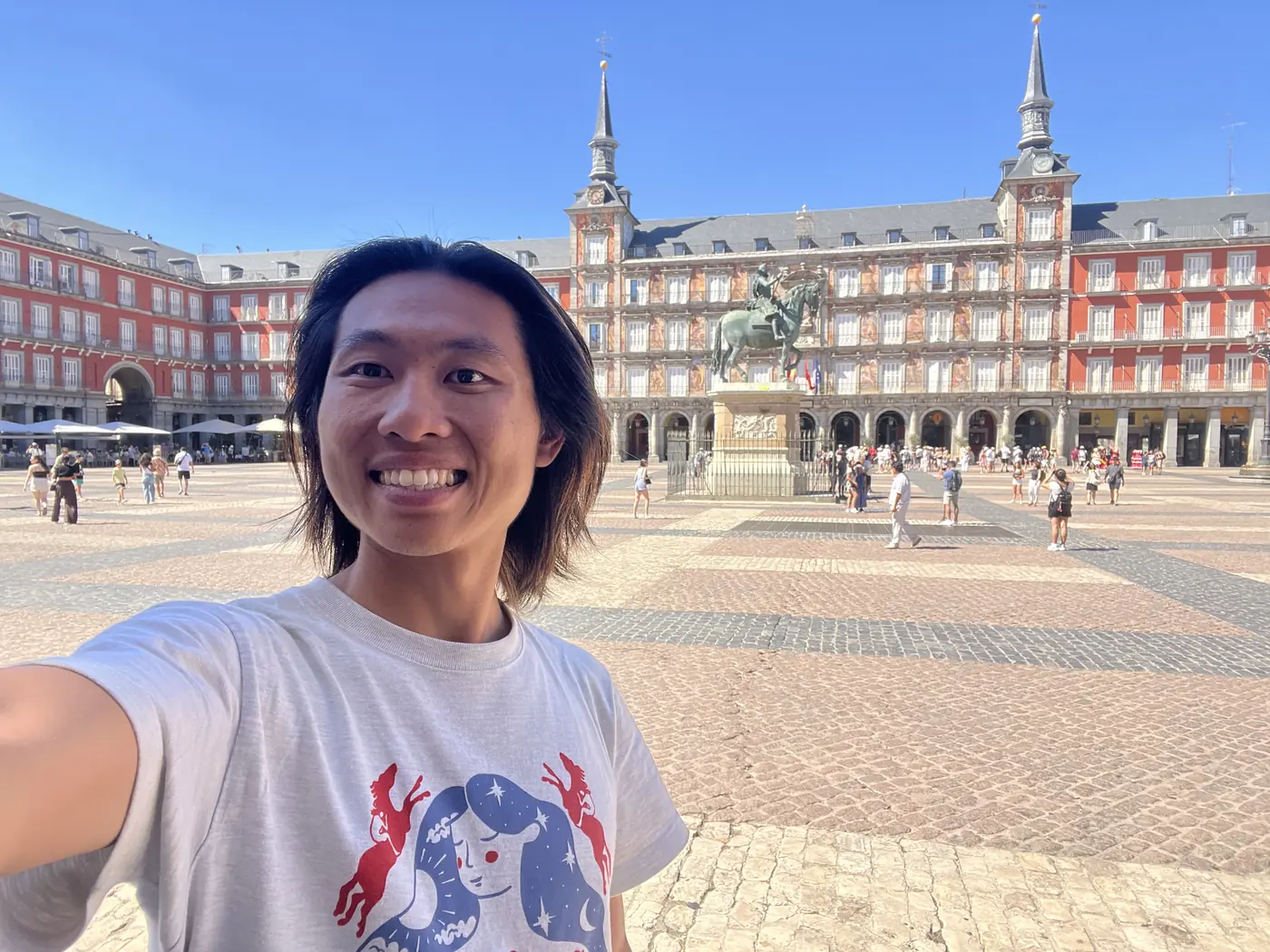 Shin selfie in Plaza Mayor, Madrid, with the red facade and twin spires of the Casa de la Panadería behind him