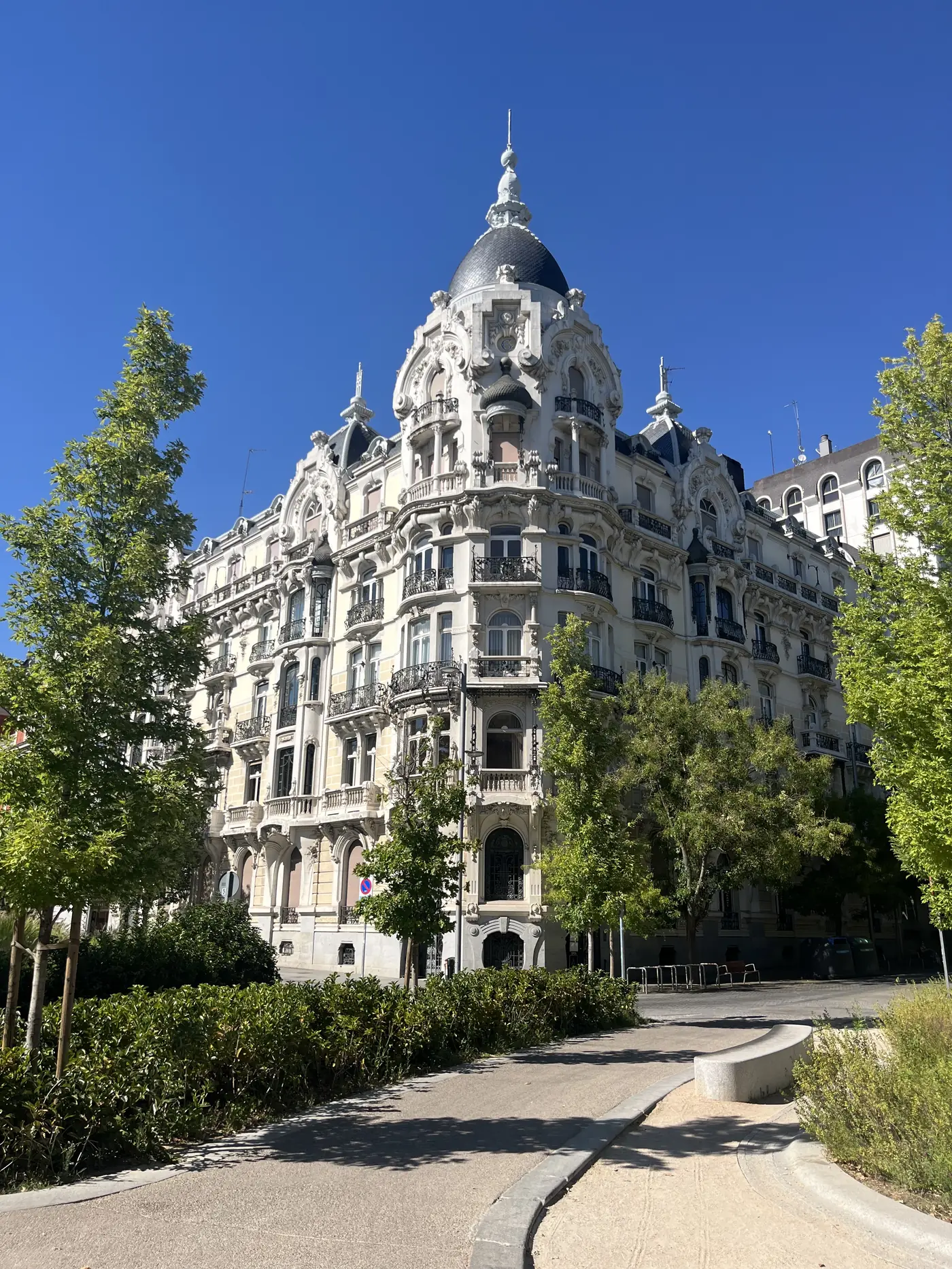 An ornate Belle Époque corner building near Paseo de Recoletos in Madrid, with a domed turret roof and carved stone balconies
