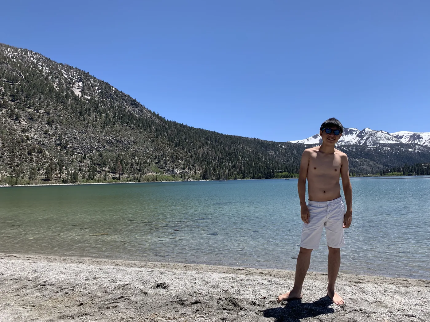 Standing at an alpine lake with turquoise water and snow-capped Sierra peaks
