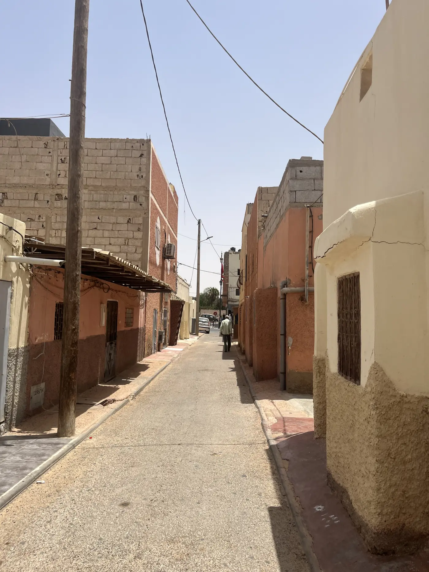 A quiet residential alley in Laayoune with sand-coloured concrete-block buildings and a person walking in the distance