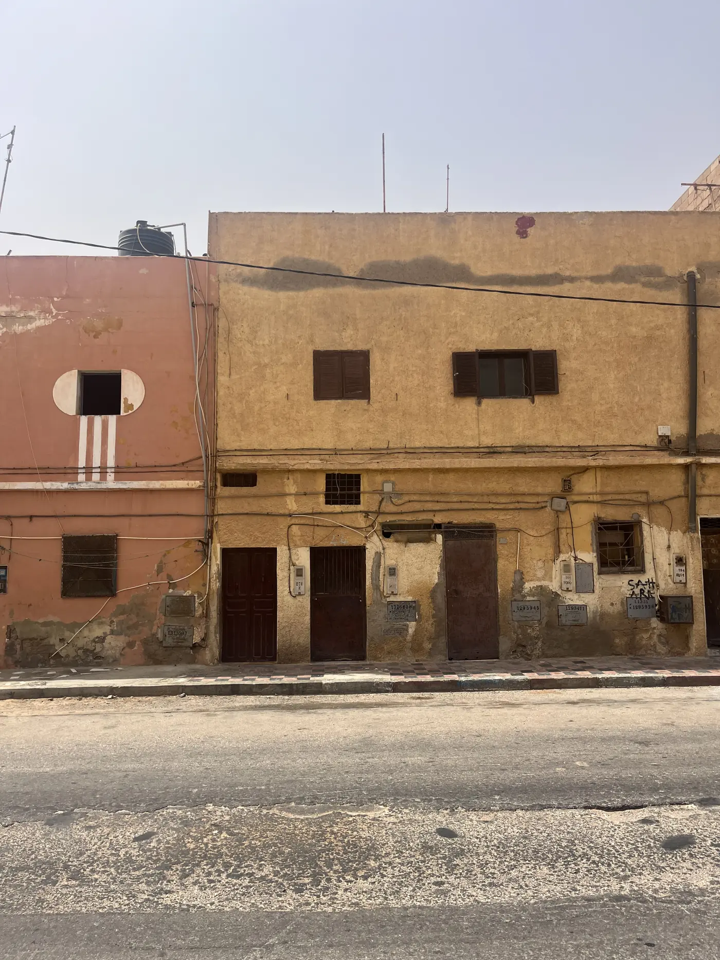 A weathered ochre-coloured Spanish colonial-era building on a quiet street in Laayoune, shuttered windows and old wiring
